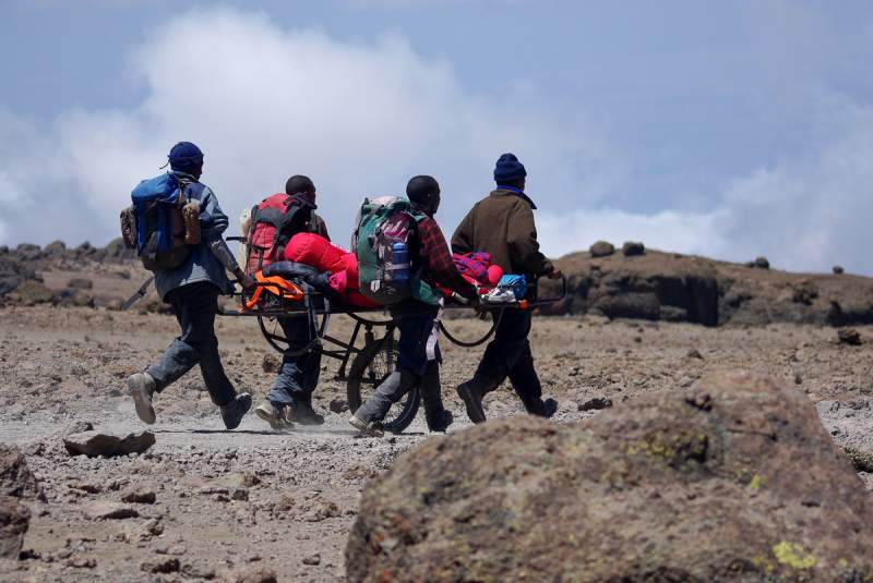 Průvodci snášejí člověka trpící na horskou nemoc. Kilimandžáro