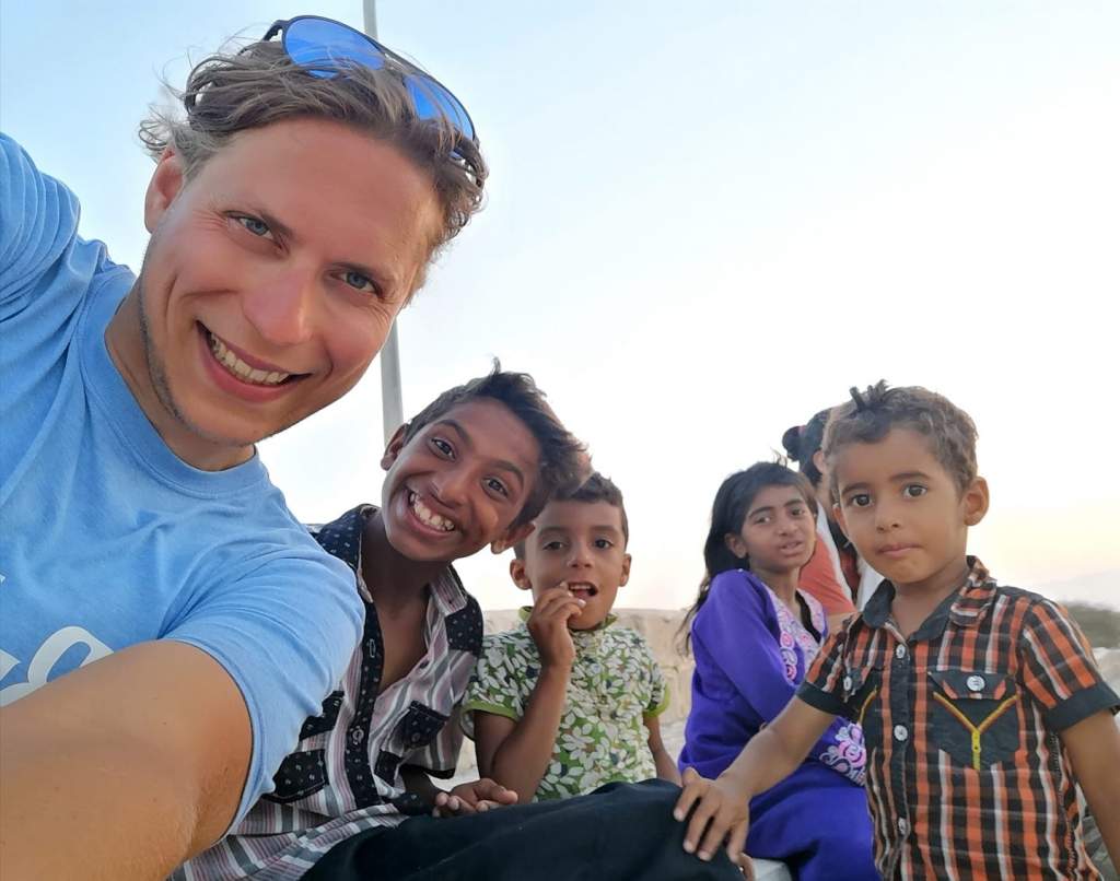 Vladimír Váchal se usmívá a fotí selfie s několika místními dětmi, pravděpodobně v Íránu, za jasného denního světla.