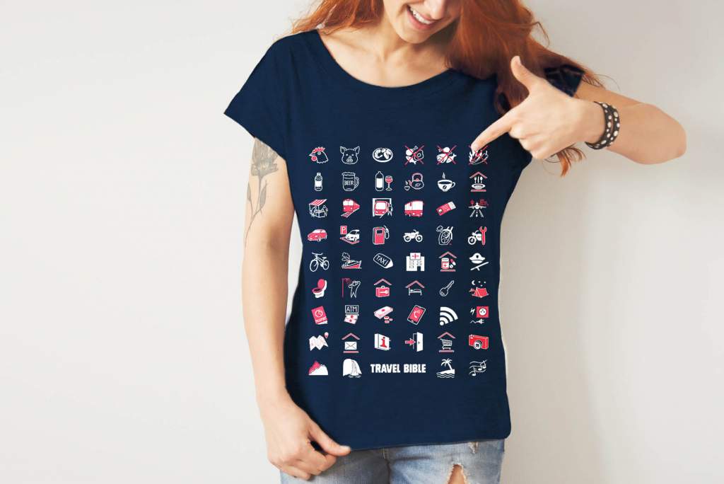Žena v tmavě modrém dámském tričku Svět s bílými a červenými cestovatelskými ikonami, ukazující na motiv ohně. Tričko s nápisem Travel Bible.