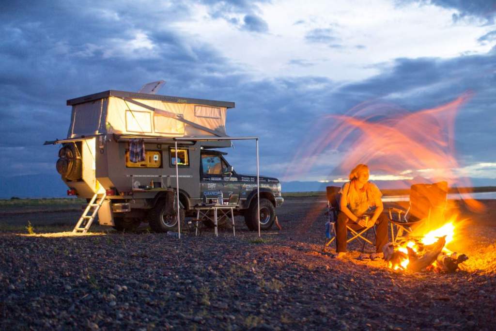 Off-road vozidlo s rooftop stanem, žena u táboráku v divočině za soumraku. Ideální pro vanlife a nezávislé cestování.