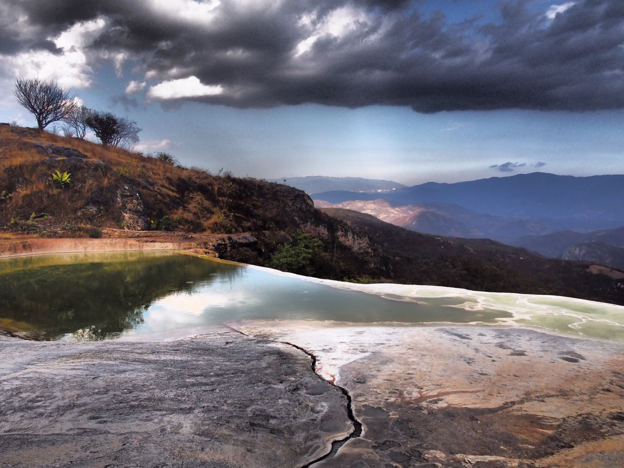 Přírodní minerální bazénky a zkamenělý vodopád Hierve el Agua v Oaxace v Mexiku pod dramatickou oblačnou oblohou s výhledem na hory.