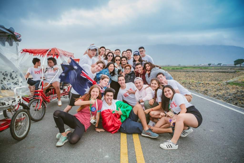 Studenti výměnného pobytu na Taiwanu s australskou vlajkou, pózující na silnici s pedálovými koly mezi poli a horami.