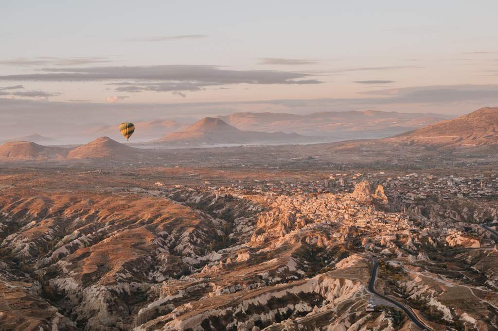 Panoramatický pohled na skalní město Uchisar a zvlněnou krajinu Kappadokie za podzimního svítání s horkovzdušným balonem.