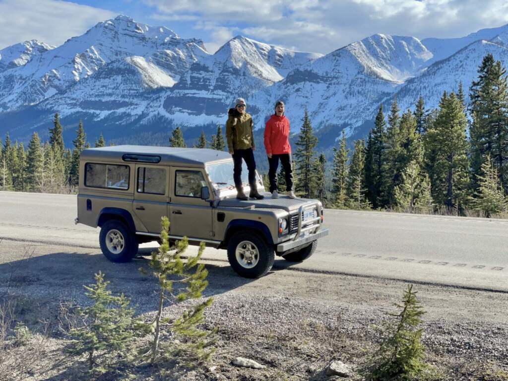 Alča a Mája na Land Roveru Defender s výhledem na zasněžené Skalnaté hory. Ideální pro road trip v Americe.