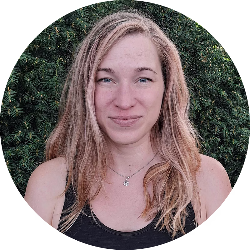 Markéta Rysavá, dobrovolnice a cestovatelka, s úsměvem. Detail obličeje a blond vlasů na pozadí zelených jehličnanů.