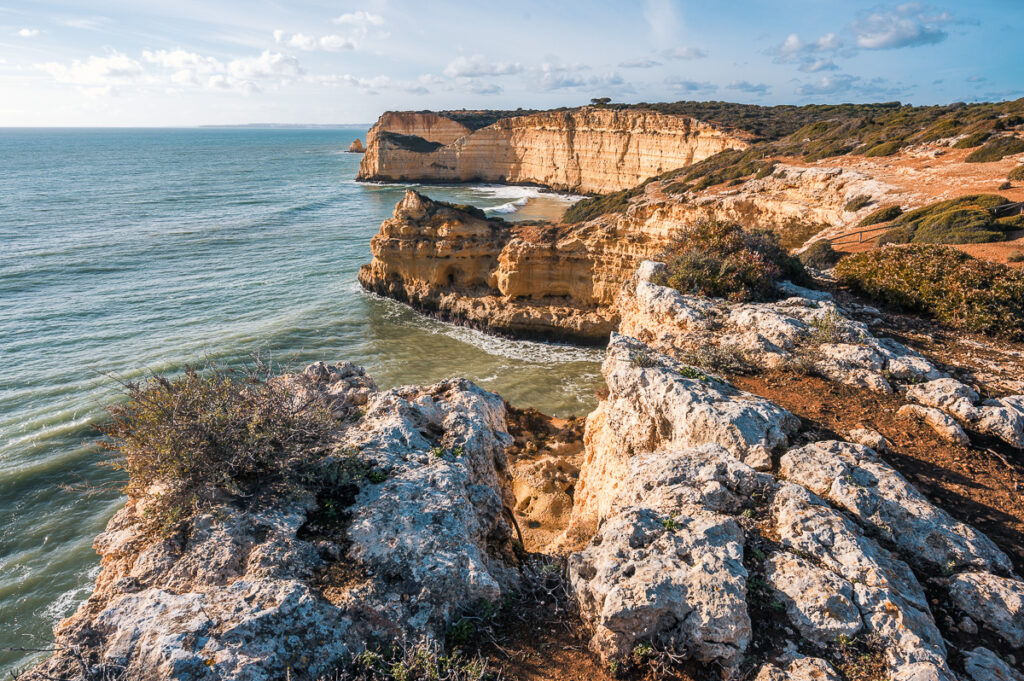 Pobřeží Algarve v Portugalsku s vysokými pískovcovými útesy a skalními formacemi omývanými Atlantským oceánem za slunečného dne.