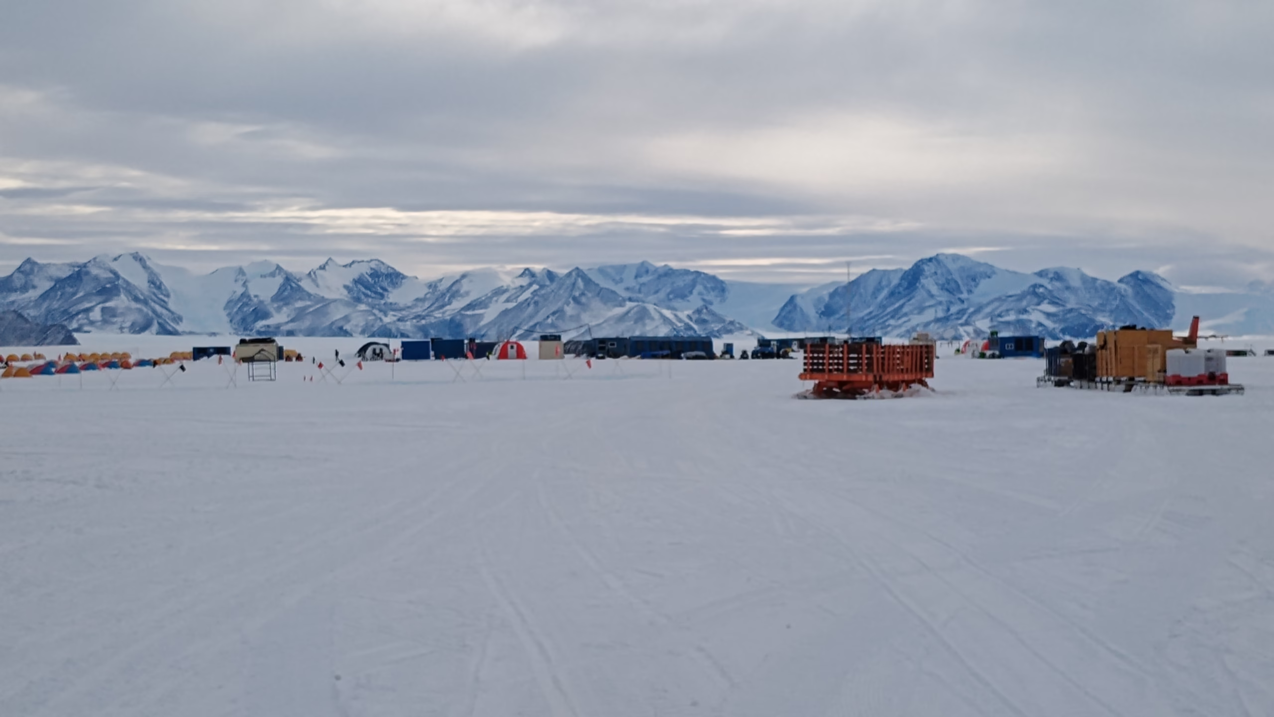 Antarktický tábor s vybavením a zasněženými horami v pozadí, Antarktida