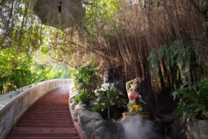 Schody vedoucí k chrámu Wat Saket v Bangkoku, s mlhou stoupající podél zábradlí a sochou ženy s hadem u vodopádu.