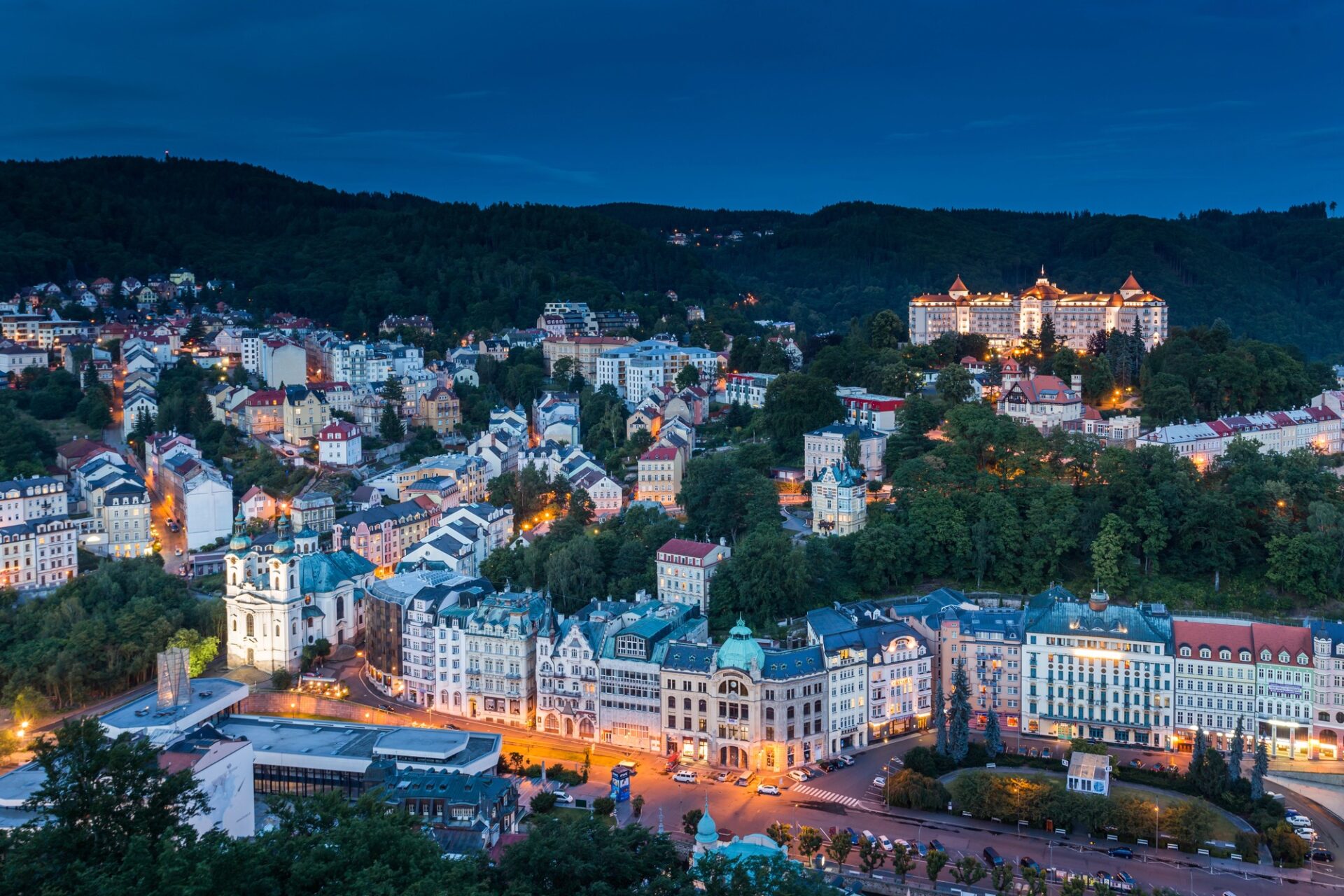 Panorama Karlových Varů za soumraku s osvětleným Hotelem Imperial nad městem