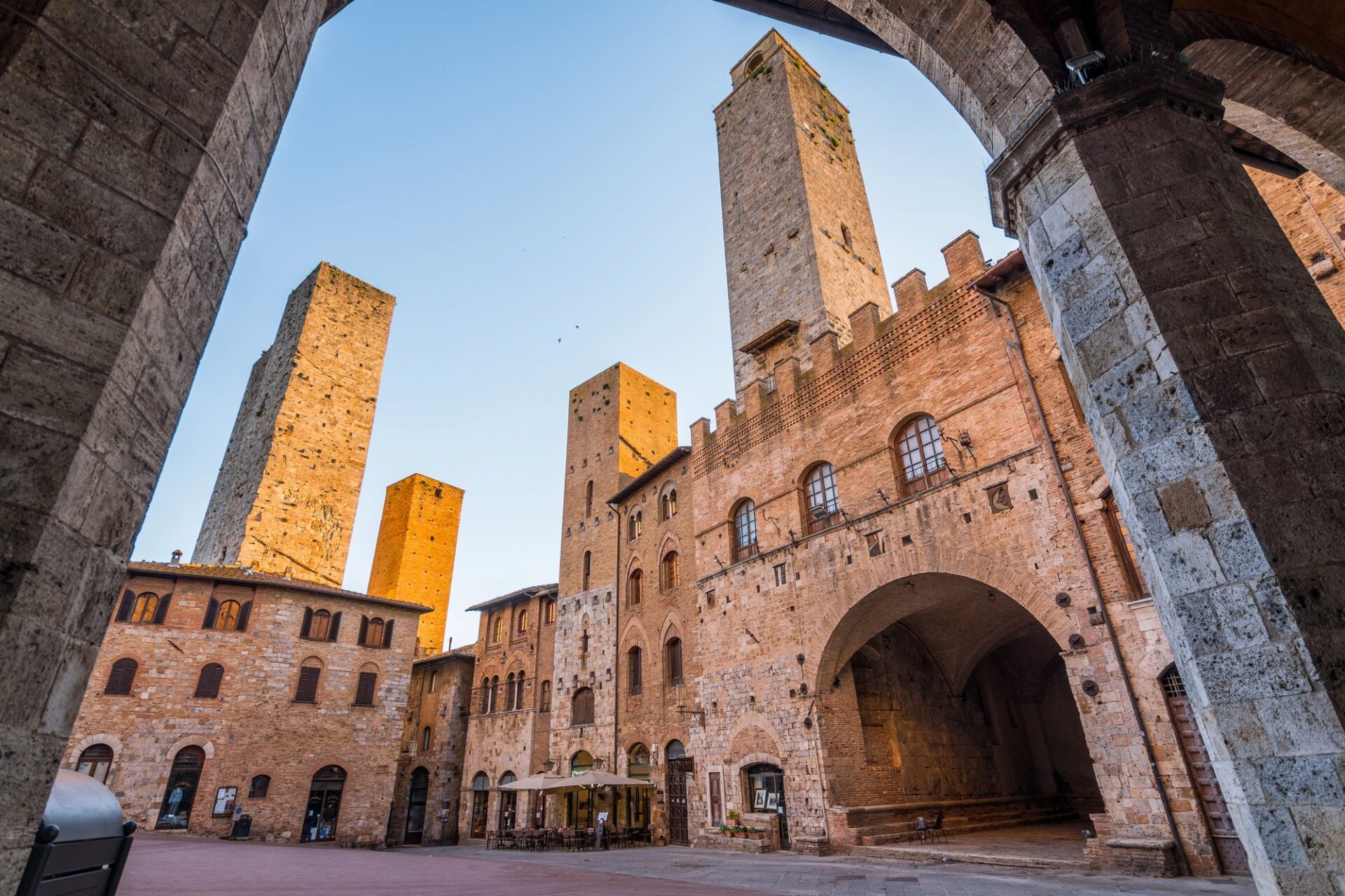 Piazza del Duomo v San Gimignanu v zlatém světle pohledem skrze kamenný oblouk