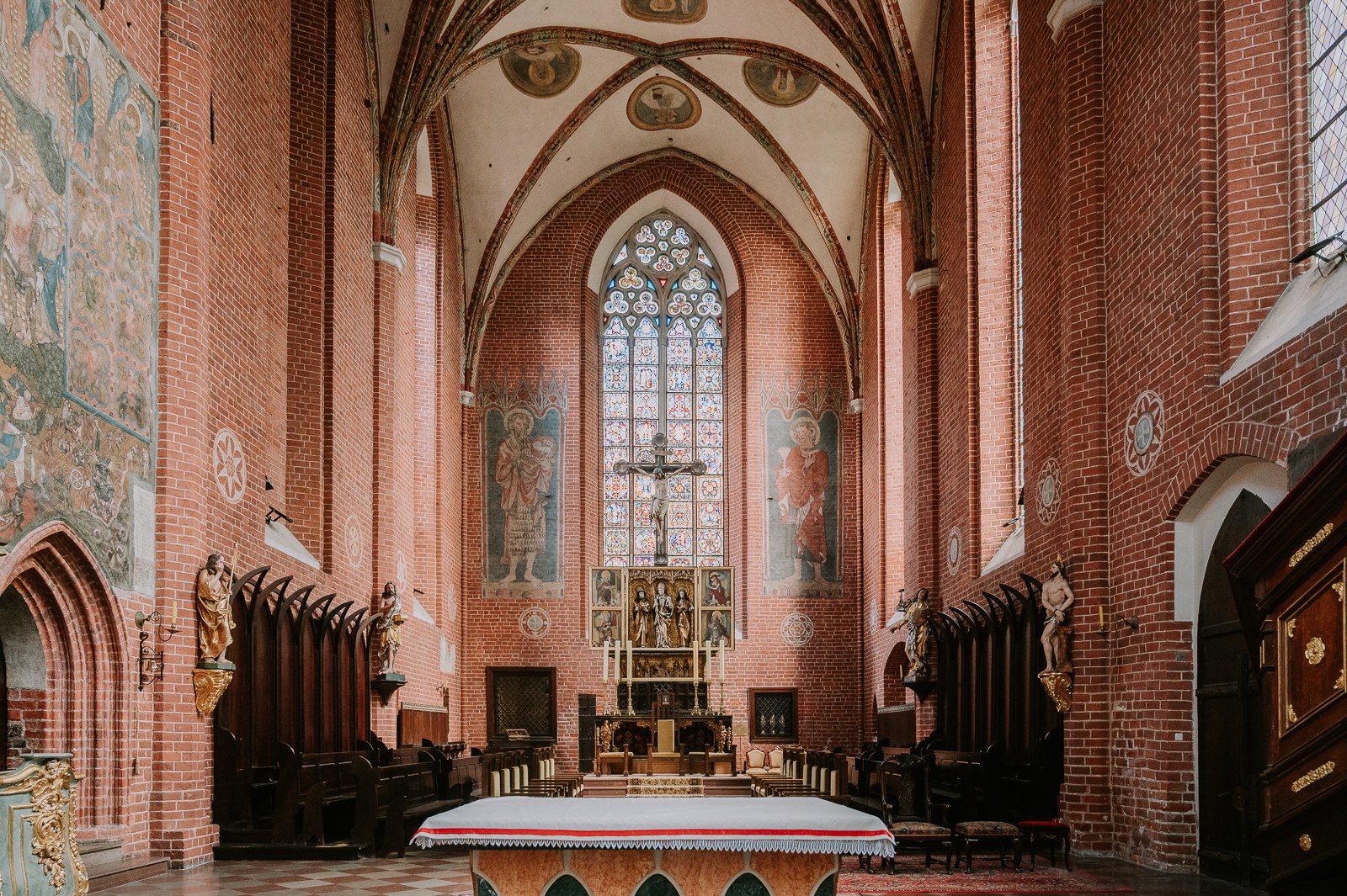 Interiér katedrály sv. Jana Křtitele a Jana Evangelisty v Toruni Gotický cihlový interiér katedrály sv. Jana Křtitele a Jana Evangelisty v Toruni s křížem a vitrážovým oknem