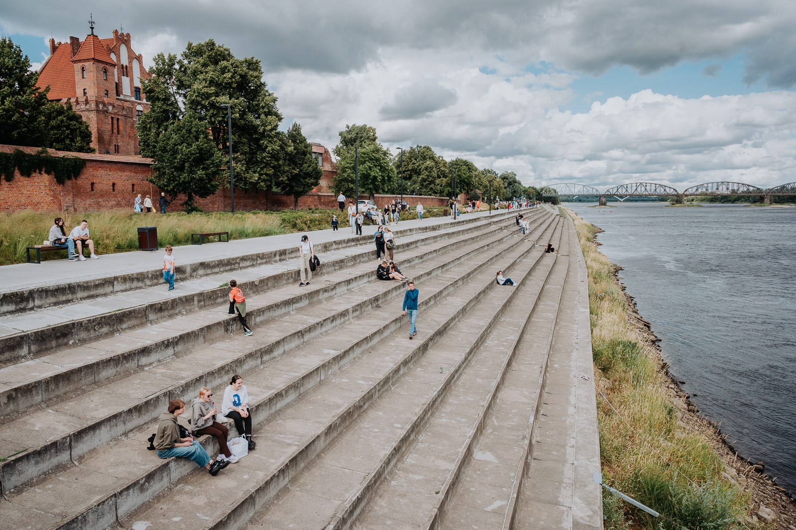 Nábřežní promenáda podél Visly v Toruni Kamenné schodovité nábřeží podél Visly v Toruni s ruinami zámku a železničním mostem v pozadí