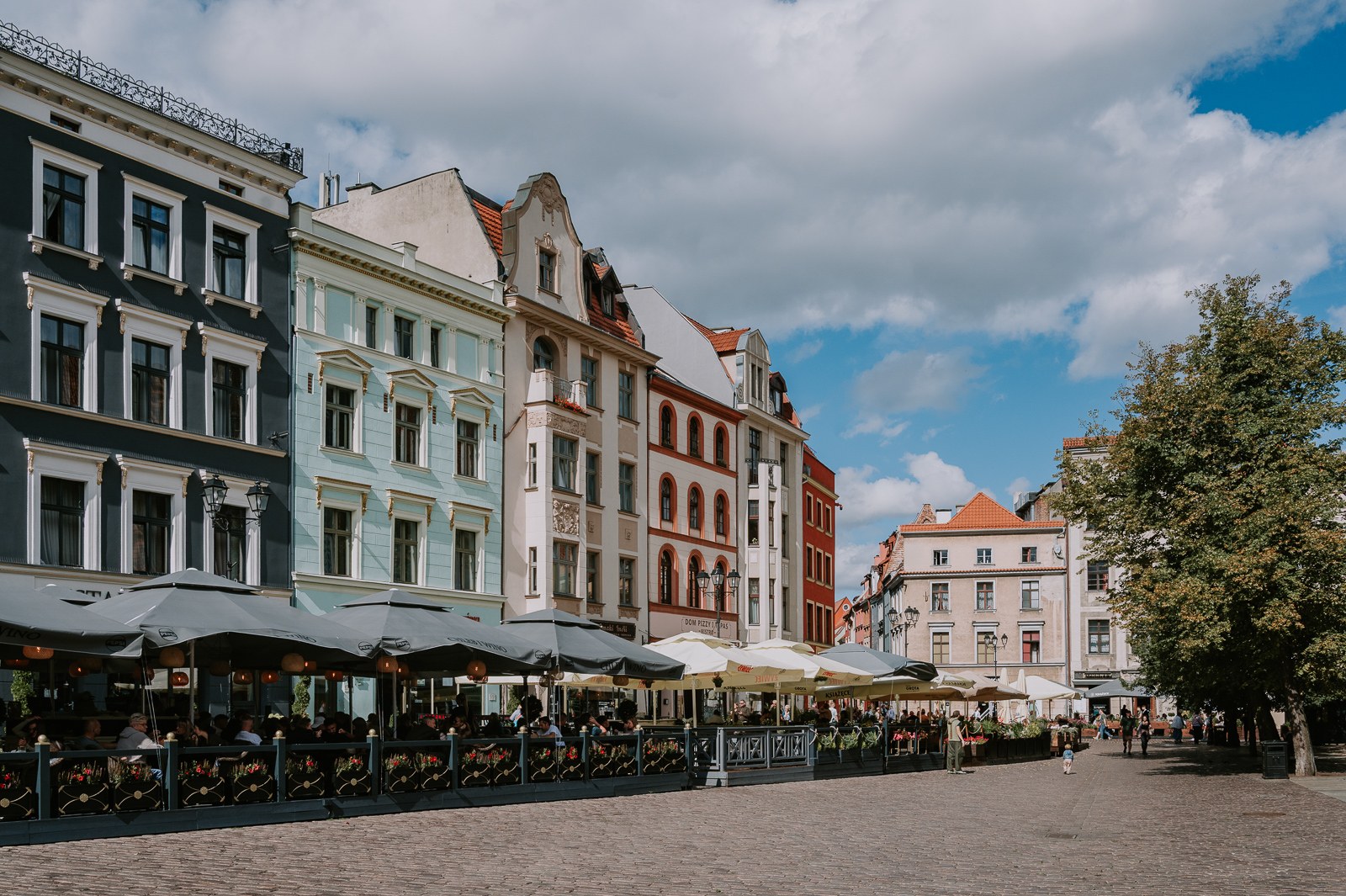 Barevné historické domy na náměstí v Toruni s venkovními posezeními restaurací