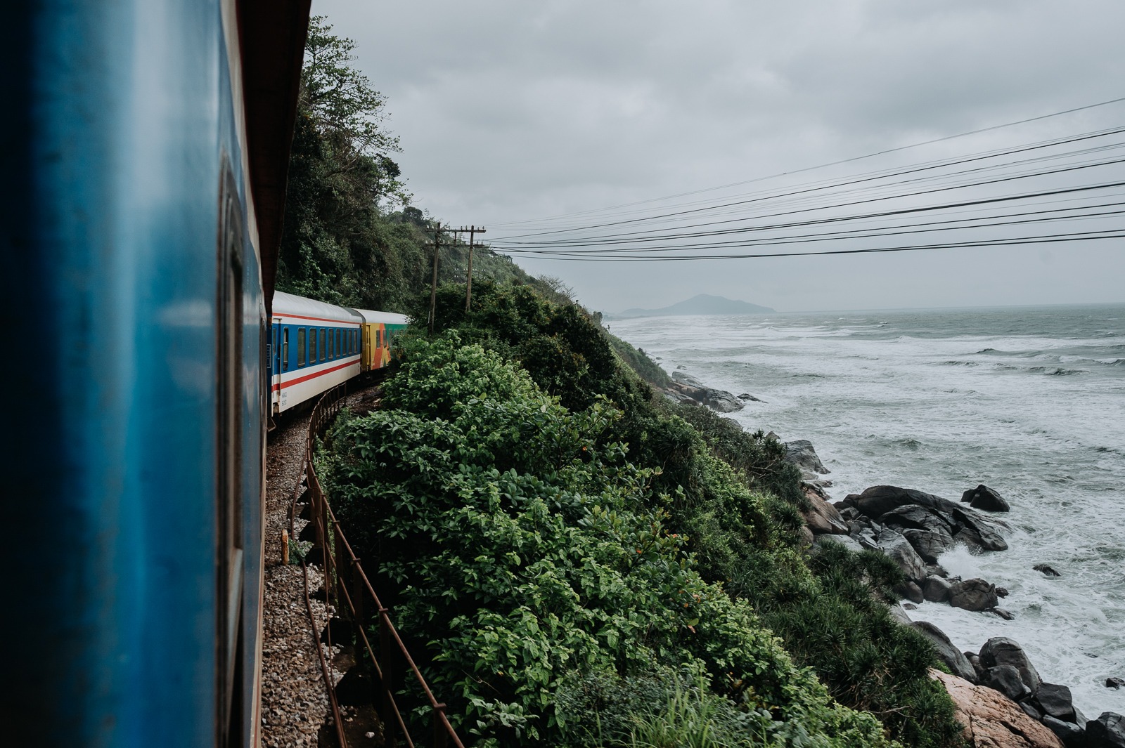Vlak Reunification Express jedoucí po pobřeží pod průsmykem Hai Van ve Vietnamu