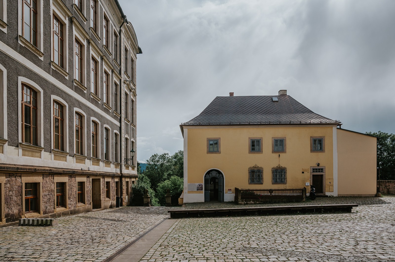 Dlážděný dvůr u broumovského kláštera s žlutou budovou