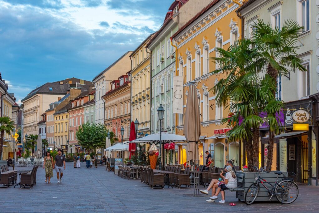 Pěší zóna Alter Platz v Klagenfurtu s pastelovými fasádami a předzahrádkami kaváren