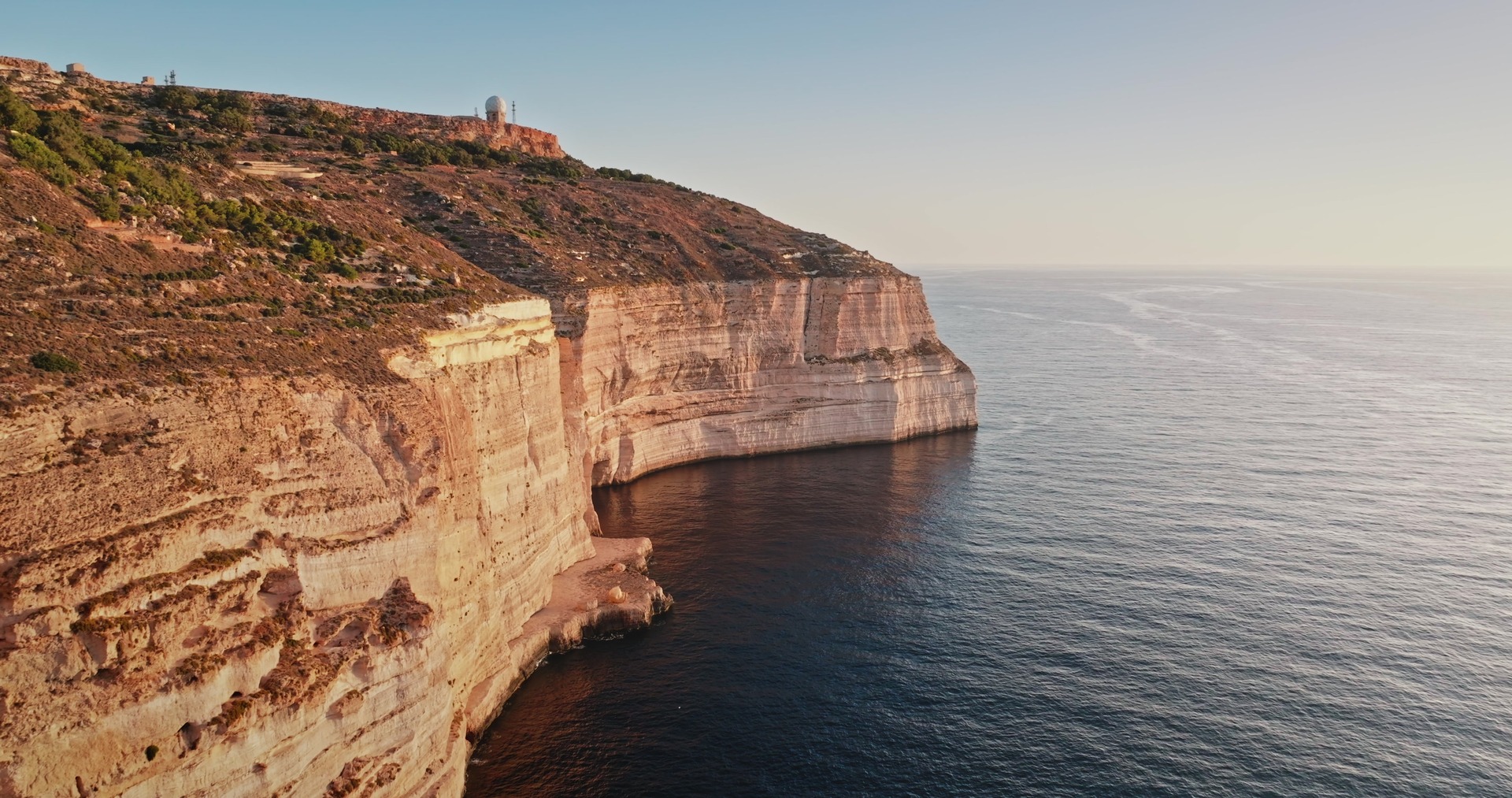 Útesy Dingli Cliffs se zlatým světlem nad klidným mořem