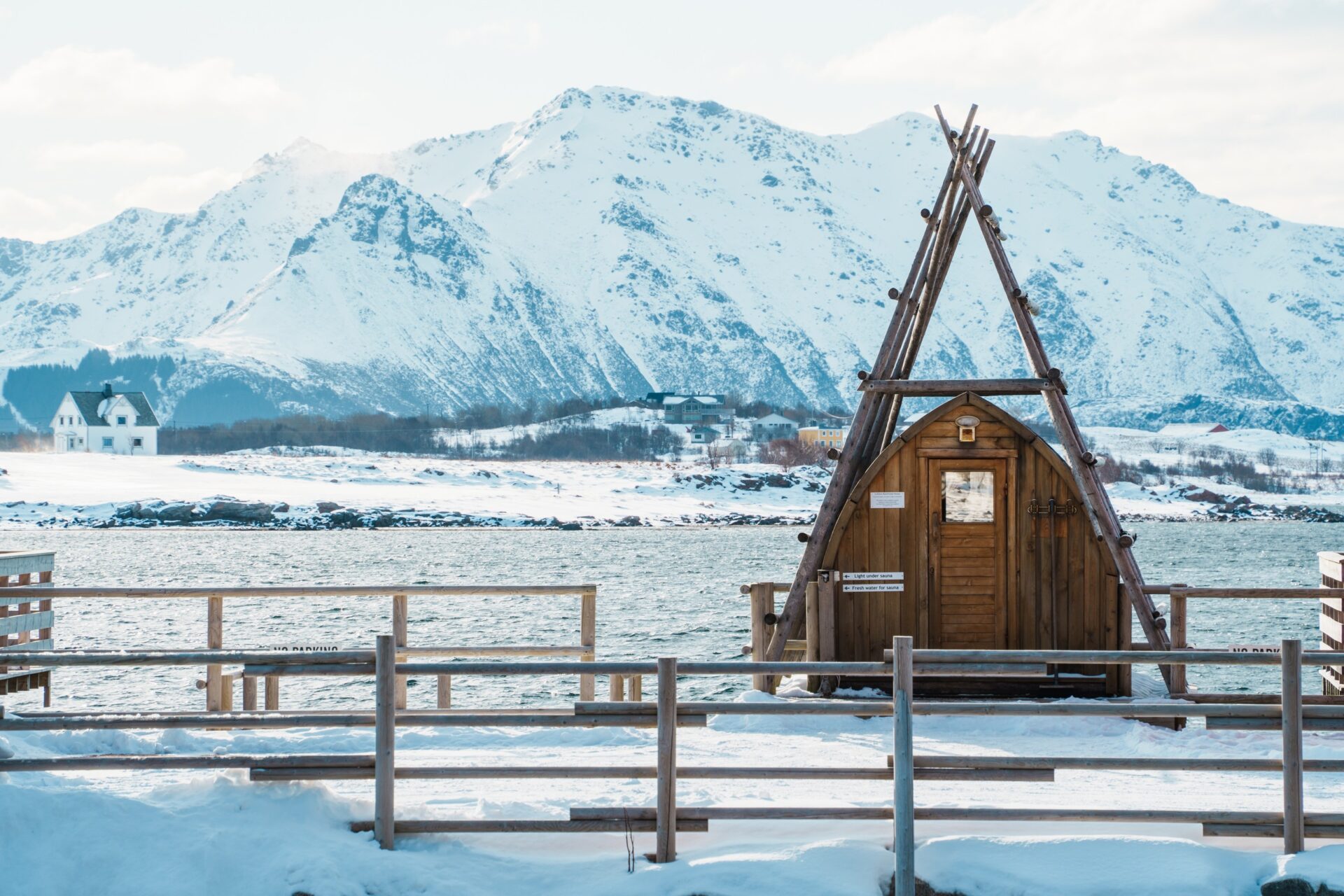 Dřevěná sauna na břehu fjordu mezi zasněženými horami