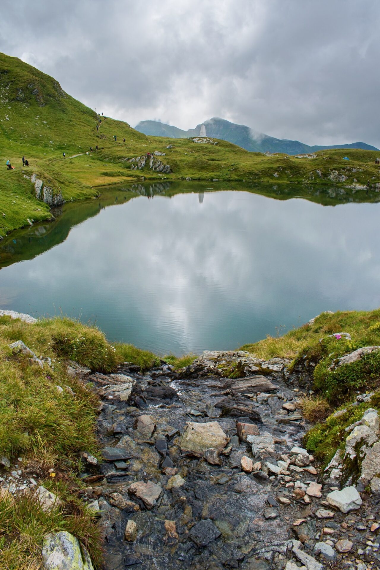 Ledovcové jezero v pohoří Făgăraș s turisty na hřebeni nad hladinou