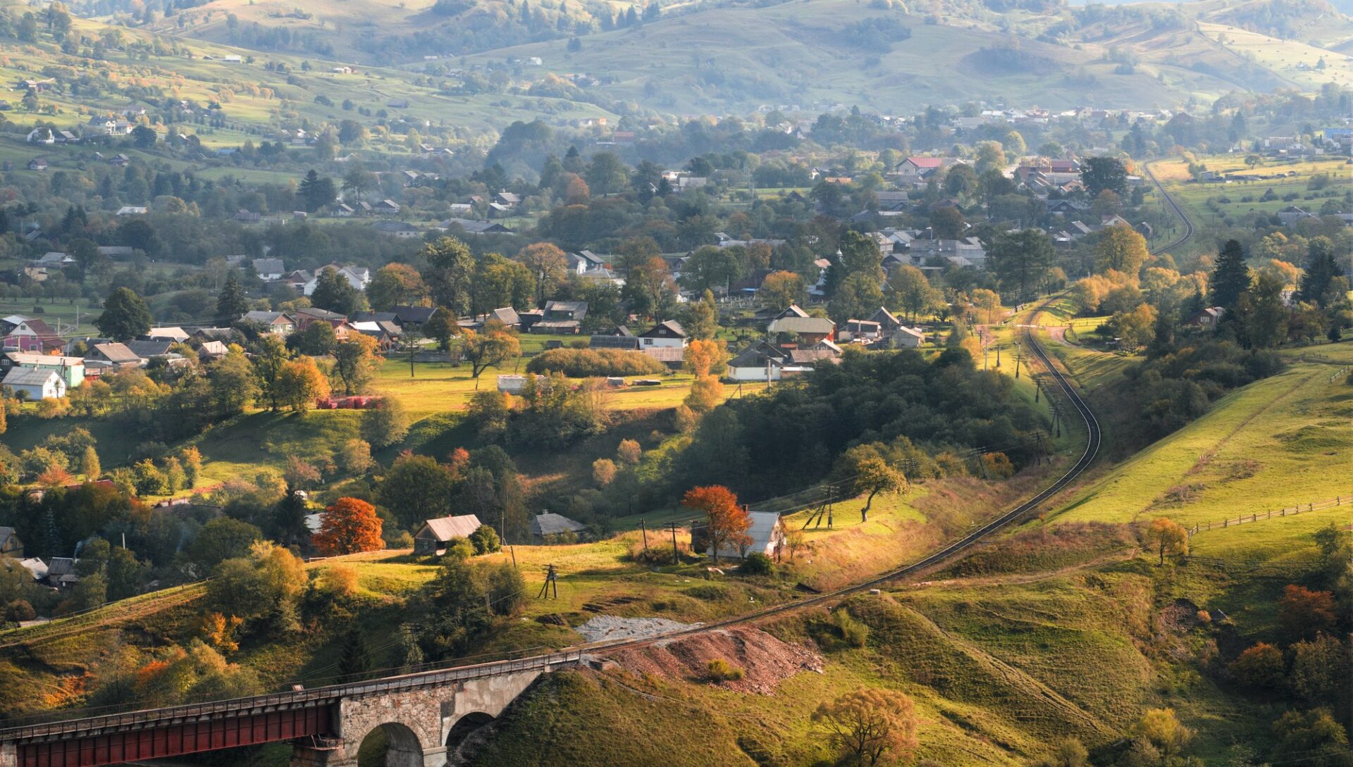 Kamenný železniční viadukt nad podzimní karpatskou vesnicí v severním Rumunsku