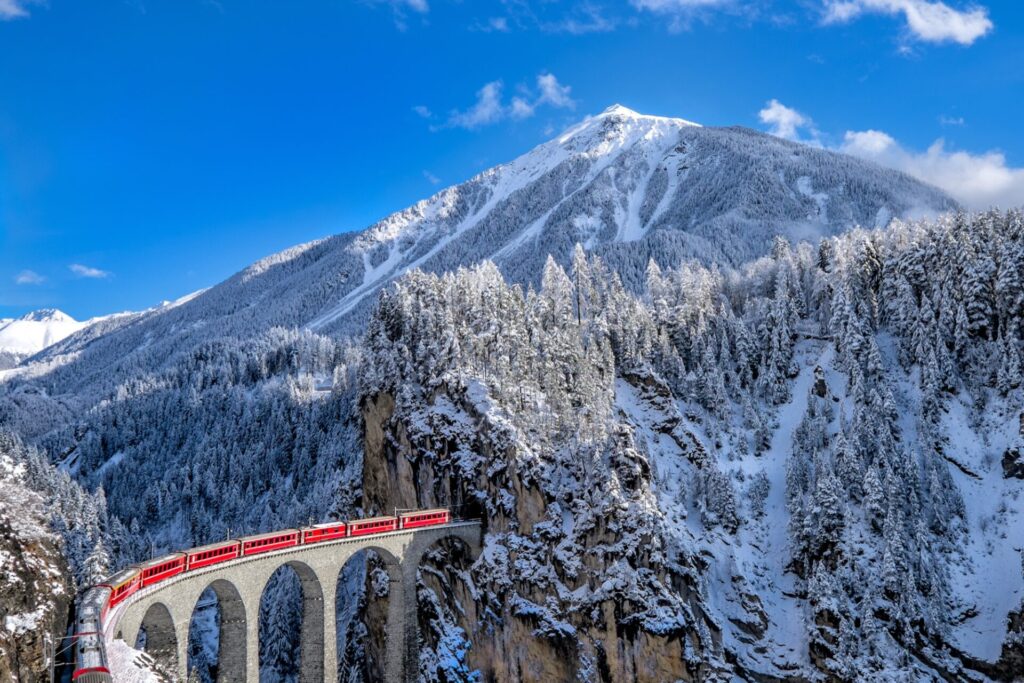 Landwasserviadukt Červený vlak Rhétské dráhy na Landwasserviaduktu v zasněžené krajině Graubündenu