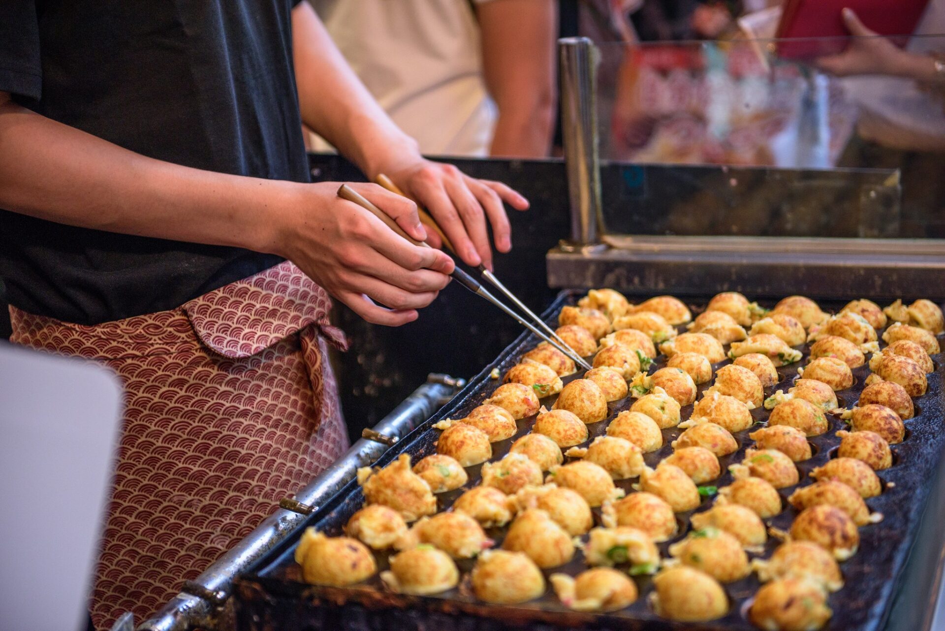 Příprava takoyaki, kuliček s chobotnicí, na rozpálené plotně u pouličního stánku