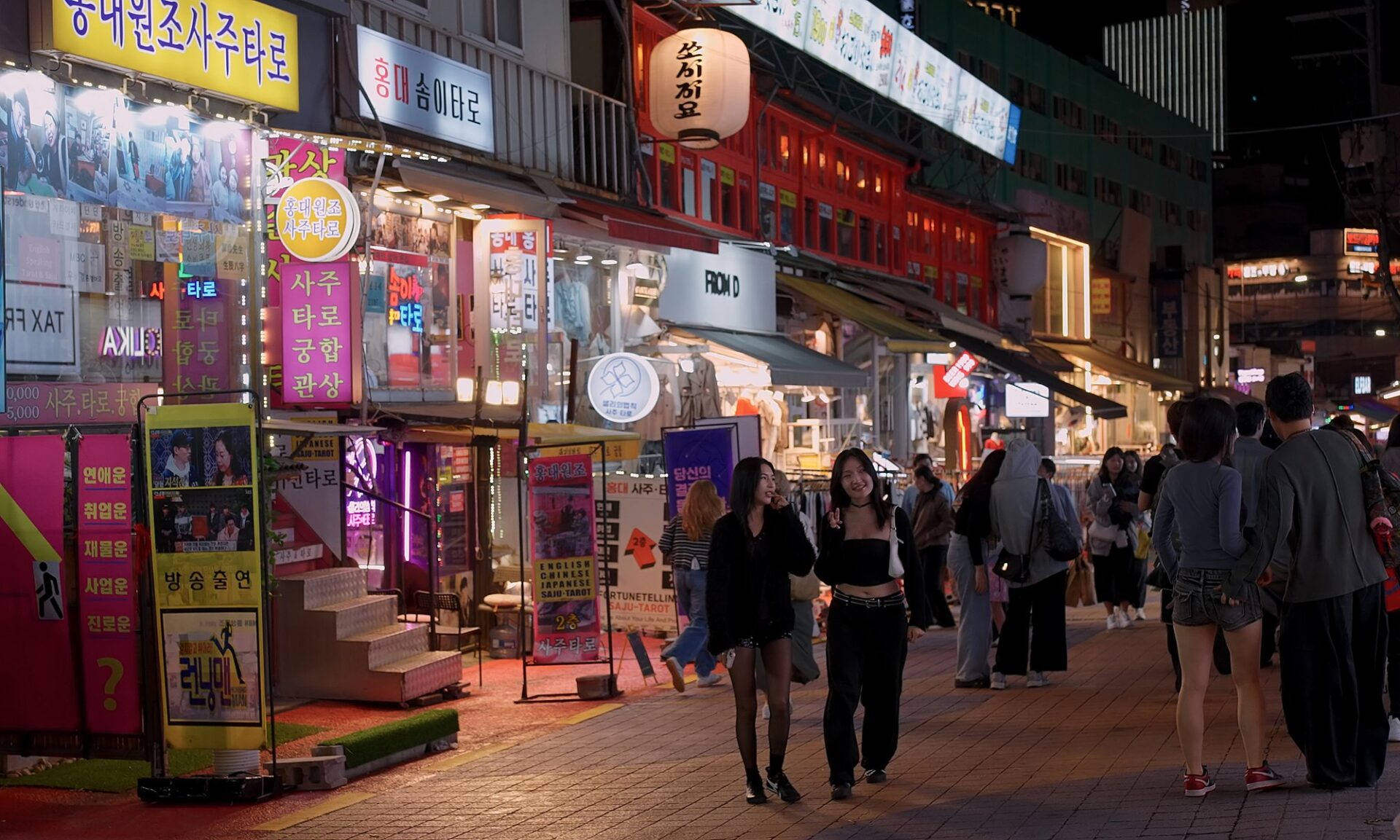 Noční ulice Hongdae v Soulu s neonovými nápisy a lidmi