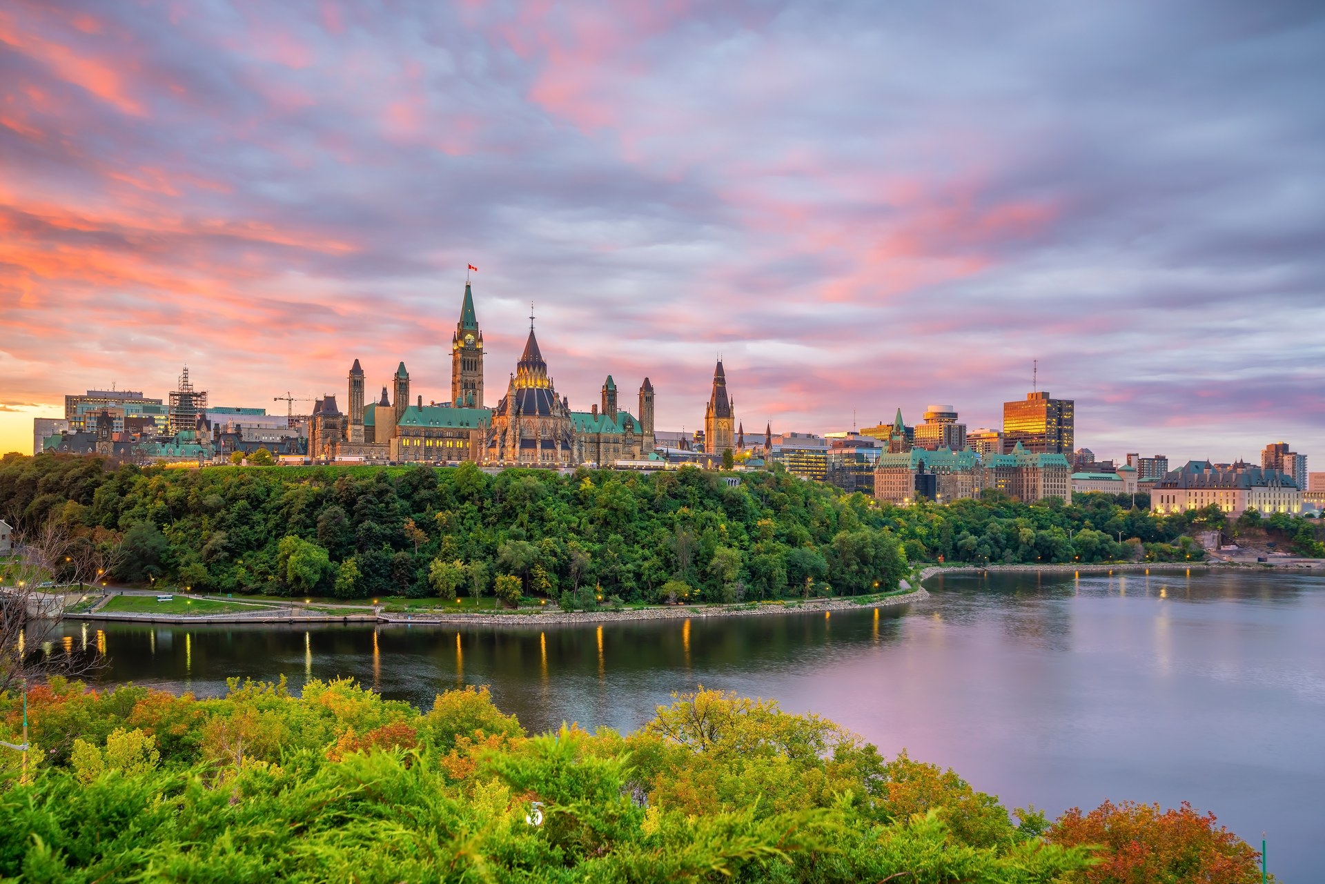 Budovy Parliament Hill nad řekou Ottawou při západu slunce