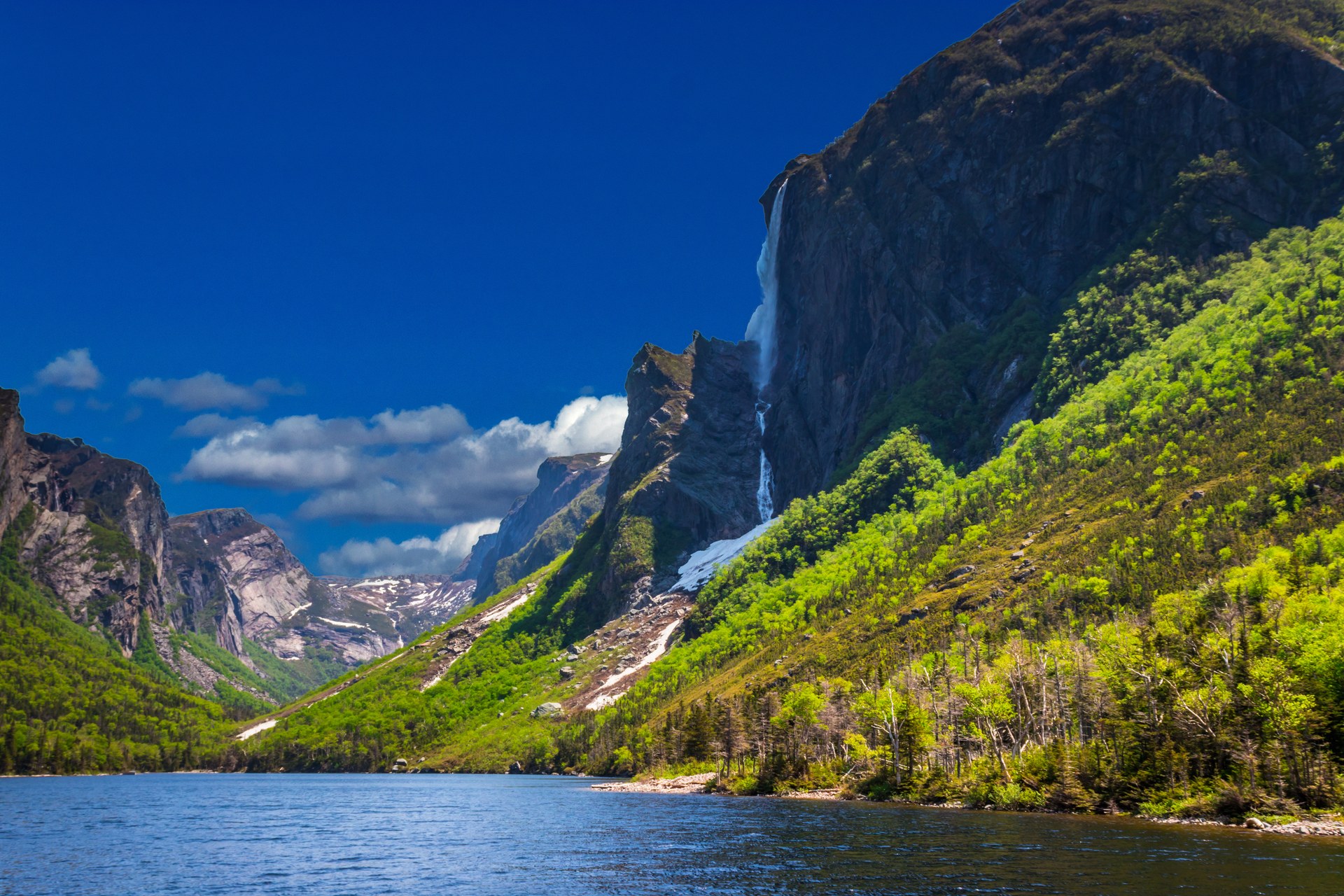 Strmé zelené skalní stěny nad vodou v národním parku Gros Morne na Newfoundlandu
